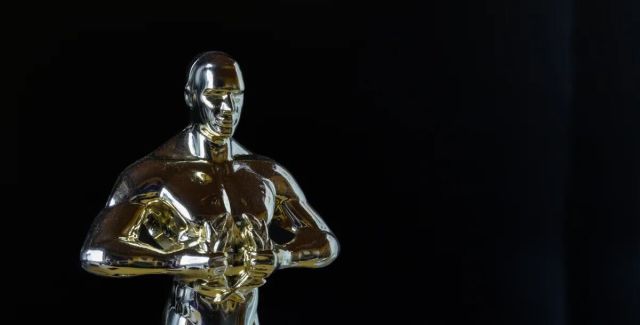 A close up photo of an Oscar award, a shiny gold statuette against a black background.