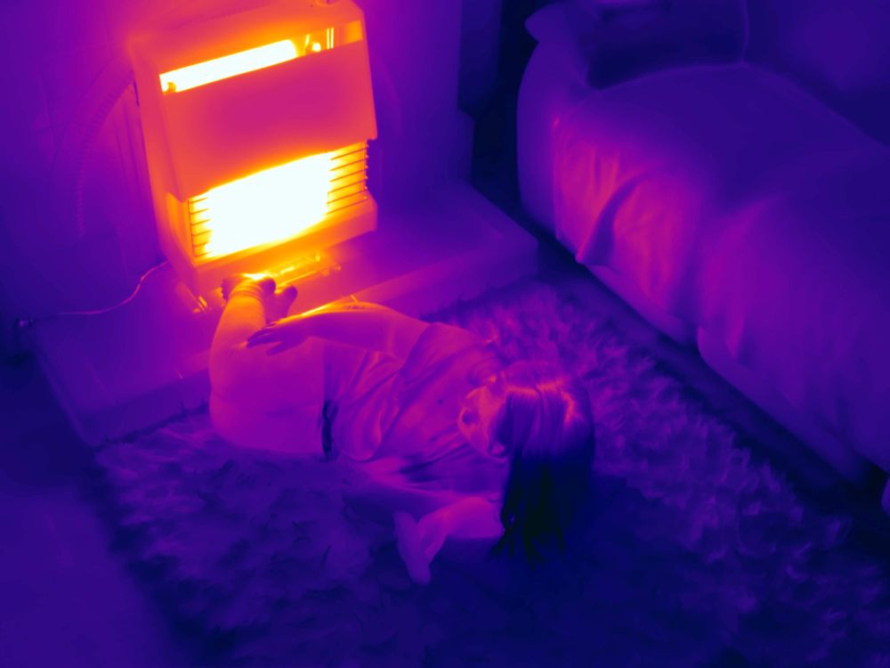 A thermal image of a girl lying on her bedroom floor with a heater glowing yellow.