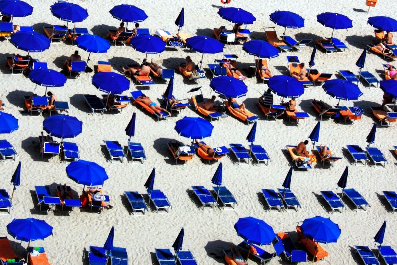 Blue sunloungers and blue umbrellas on white sands on a hot day.