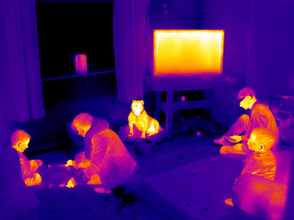 A family with two young children in their lounge, the thermal image shows a cold window and walls in the background.