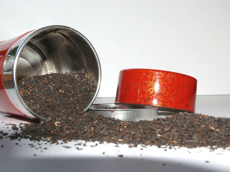 Loose tea spilling out of a red tin on its side