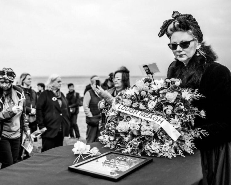 A women laying a wreath on a coffin for Lough Neagh