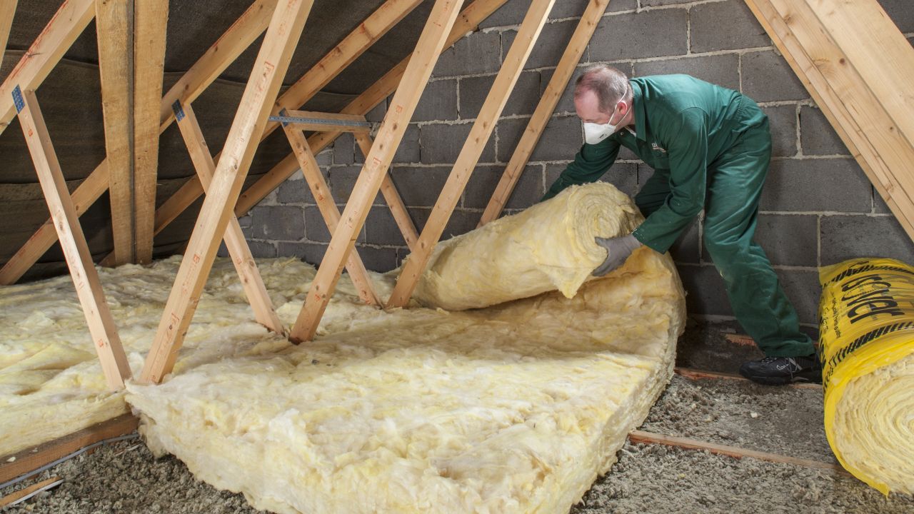 Man in overalls laying loft insulation at home