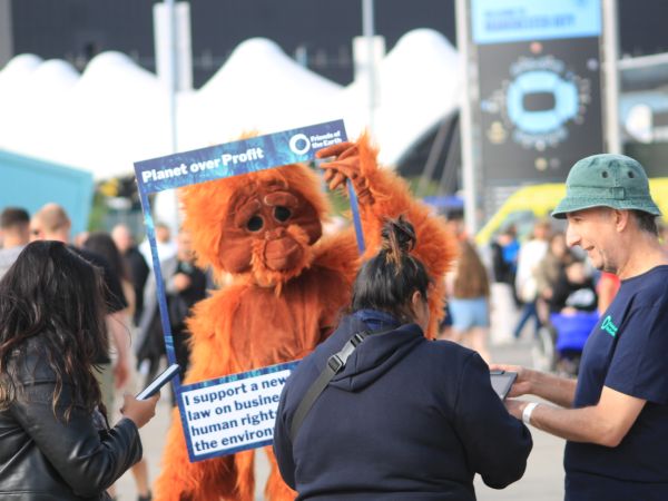 Volunteer gathering petition signatures from two concert goers, while another volunteer in an orangutan costume holds a selfie placard that reads "I support a new law on business, human rights and the environment"