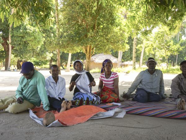 6 community members of different ages, from young to elderly sitting down on blankets facing the camera