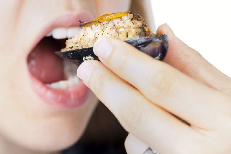 Close-up of a woman's hand and mouth as she eats a dressed mussel from its shell