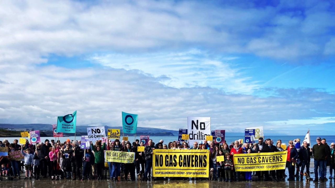 Group of people on a beach with banners that say No Gas Caverns