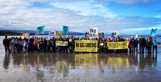 A group of people on a beach with No Gas Cavern signs