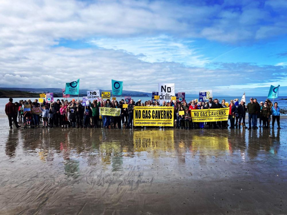 A group of people on a beach with No Gas Cavern signs