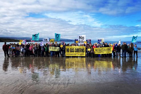 A group of people on a beach with No Gas Cavern signs