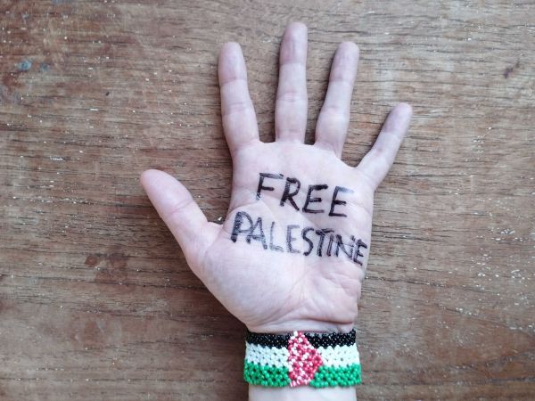 A hand with "Free Palestine" written on it and wearing a Palestinian flag bracelet