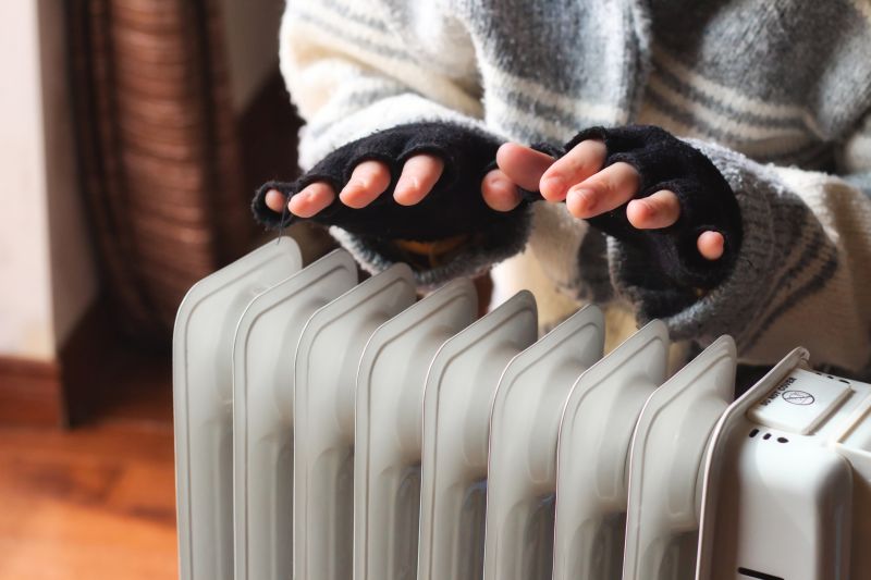 Person wearing fingerless gloves and a thick jumper, heating their hands over a radiator
