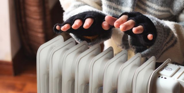 Person wearing fingerless gloves and a thick jumper, heating their hands over a radiator