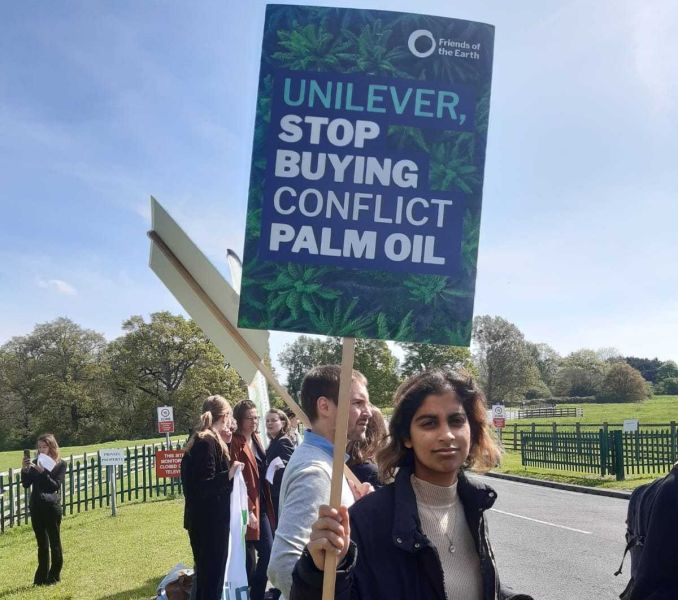 Person at a demonstration holding a placard that reads "Unilever, stop buying conflict palm oil"