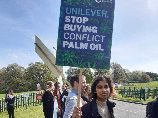 Person at a demonstration holding a placard that reads "Unilever, stop buying conflict palm oil"