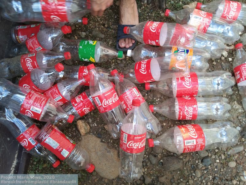 Camera focussing directly on the ground, birds-eye view of many coca-cola plastic bottles collected together on the ground
