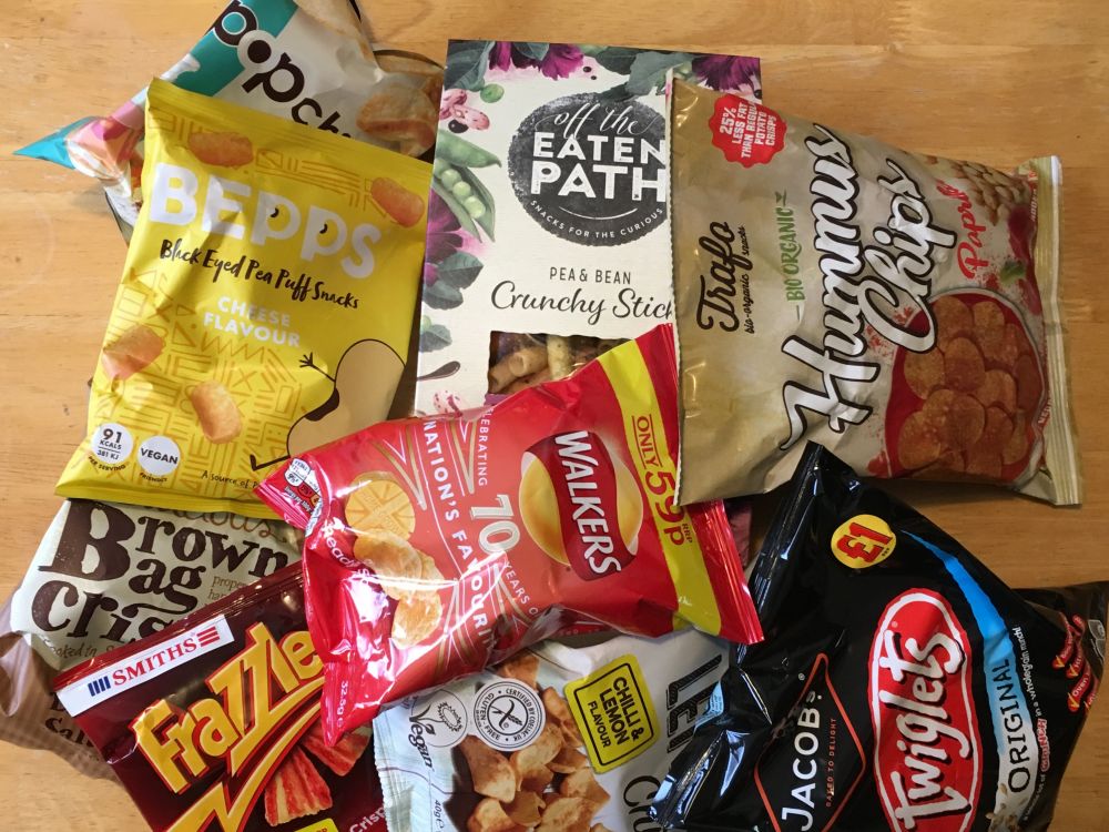 An assortment of plastic crisp packets and other snacks including Frazzles, Twiglets and Hummus Chips