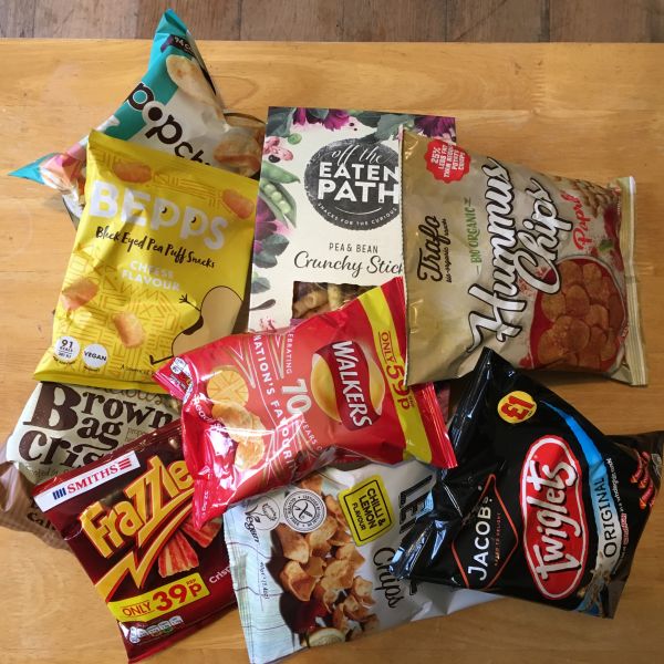 An assortment of plastic crisp packets and other snacks including Frazzles, Twiglets and Hummus Chips