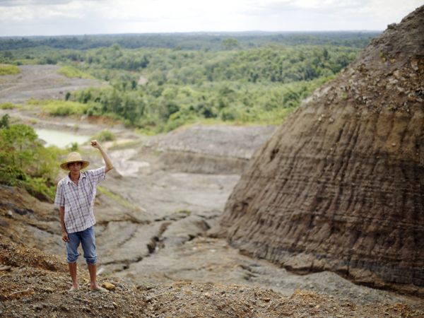 A young man wearing straw hat holding his fist in the air. He is standing among beautiful nature, alone.