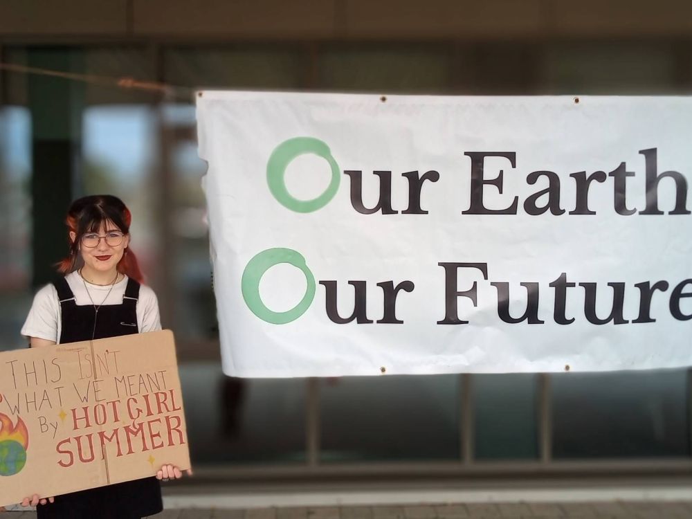 Student holding a placard saying This isn't what we meant by hot girl summer.