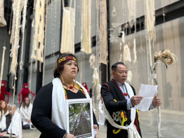 Two Indigenous leaders at the Tate Modern, one giving a speech, the other holding a photo of deforestation