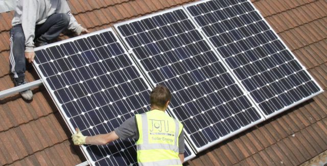 Two solar power engineers fitting solar electricity panels to a roof in North London, UK, 2011. 