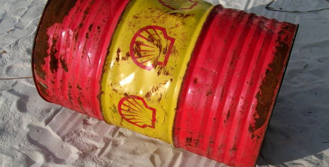 A large, empty shell oil can on a sandy beach. It's covered in oil and looks dirty.
