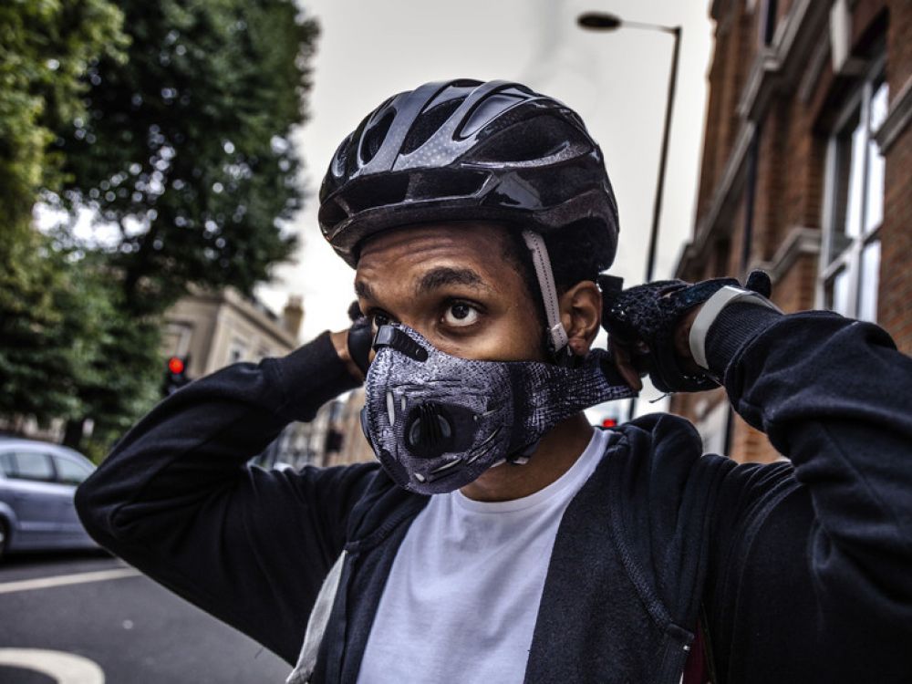 Male cyclist wearing helmet in street putting on anti-pollution mask .
