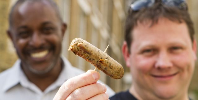 Two smiling protein-loving men hold a vegetarian sausage