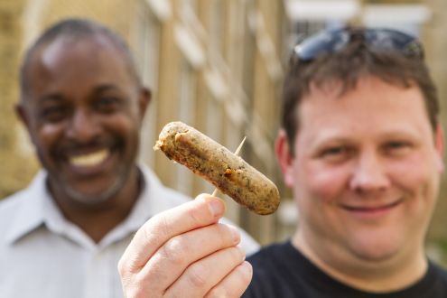 Two smiling protein-loving men hold a vegetarian sausage
