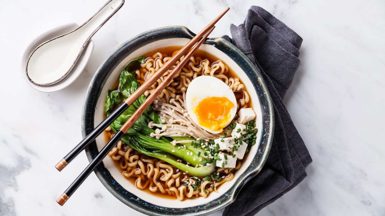 A bowl of noodles with broth, vegetables, and half a boiled egg.