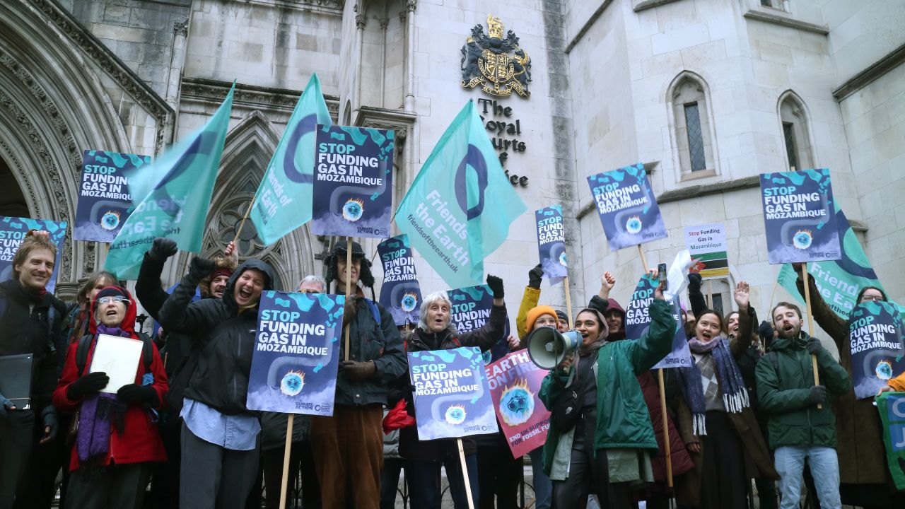 A group of climate protesters of different ages and ethnicities standing outside the Royal Courts of Justice with placards reading "Stop funding gas in Mozambique"