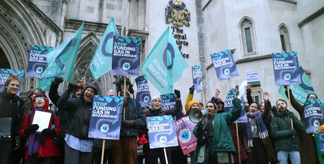 A group of climate protesters of different ages and ethnicities standing outside the Royal Courts of Justice with placards reading "Stop funding gas in Mozambique"