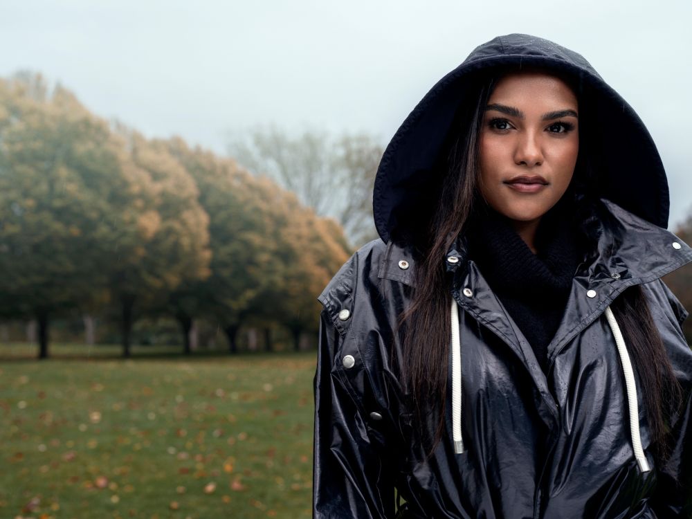 Saffron Hocking stands in the foreground wearing a raincoat, with a park and trees in the background