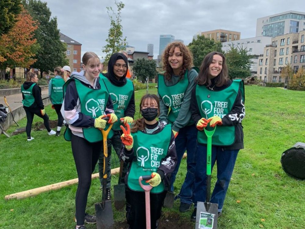 A group shot of students planting trees. They're holding spades and smiling.