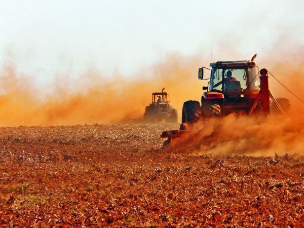 Two tractors clearing the soil for soy farming in Brazil, generating lots of dust over barren land