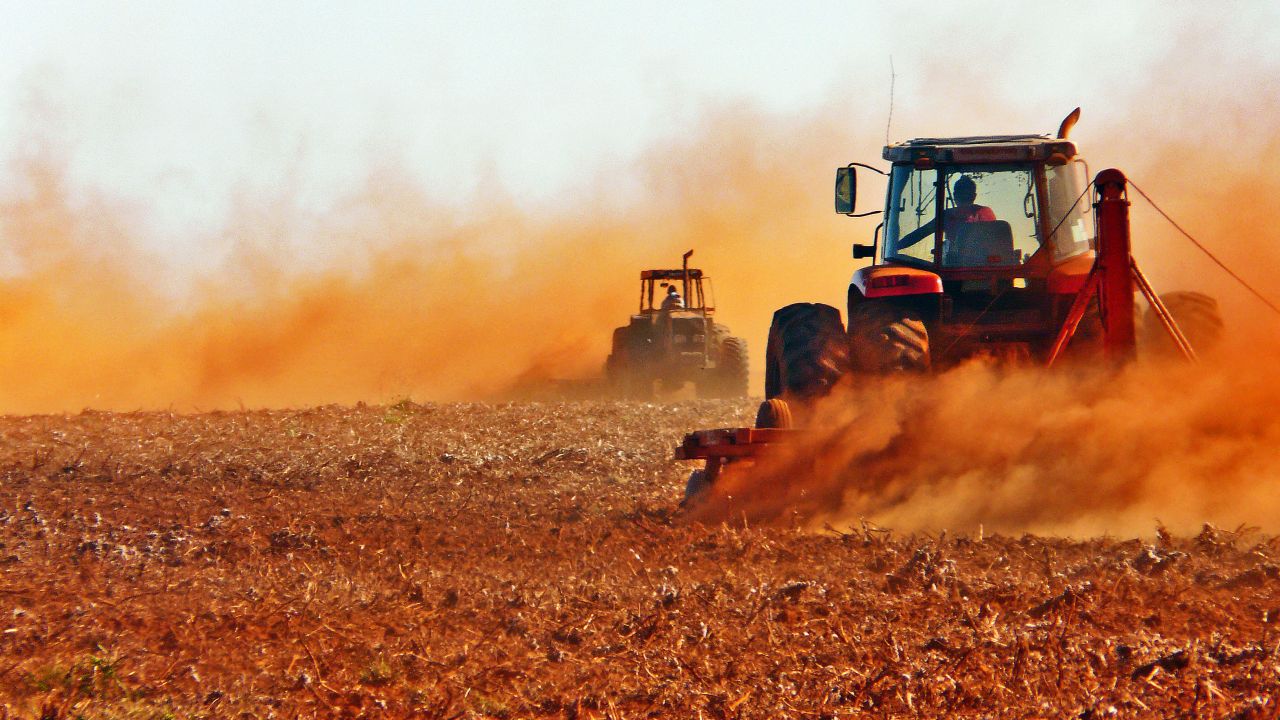 Two tractors clearing the soil for soy farming in Brazil, generating lots of dust over barren land