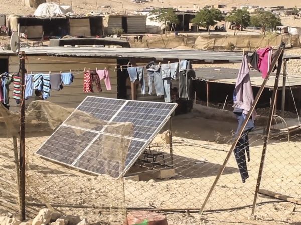 Grid electricity shown installed in a sandy, desolate village, next to clothes on a washing line
