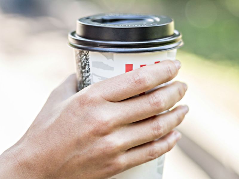 A close up of a woman's hand holding a takeaway coffee cup