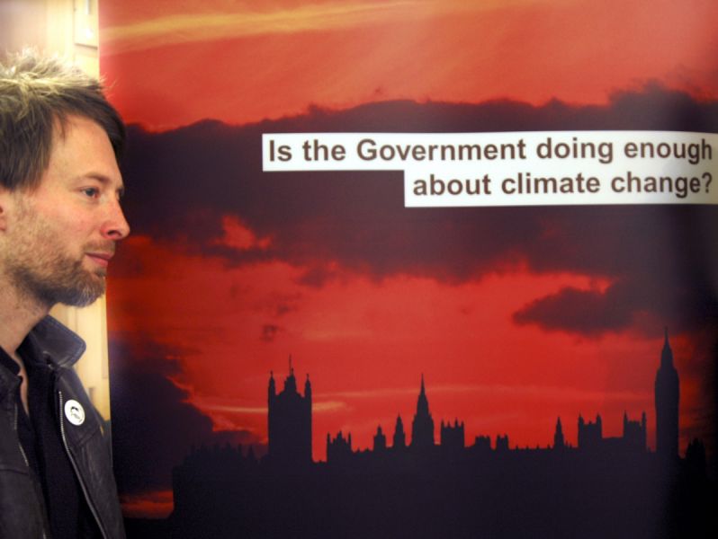 Thom Yorke standing alongside a Friends of the Earth banner which says "Is the Government doing enough about climate change?"