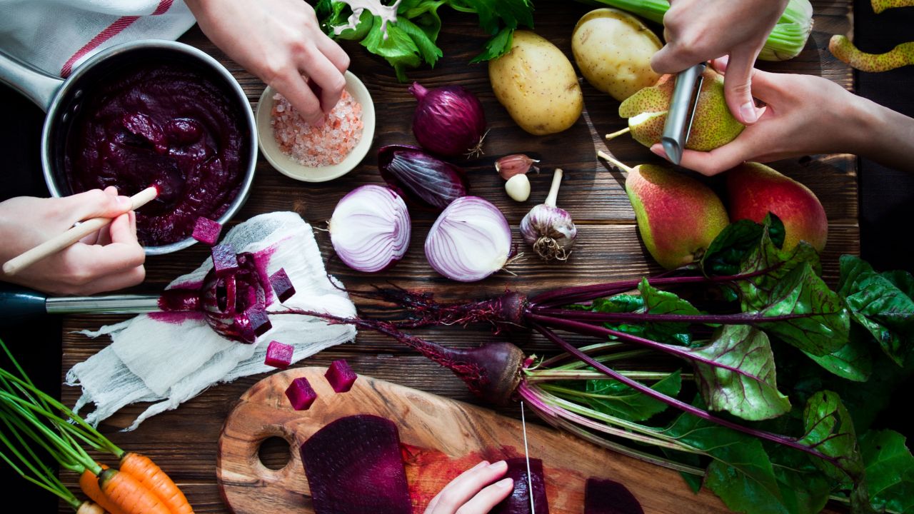 preparing vegetarian meal, chopping beets, peeling pears; potatoes, carrots and celery on a wooden board