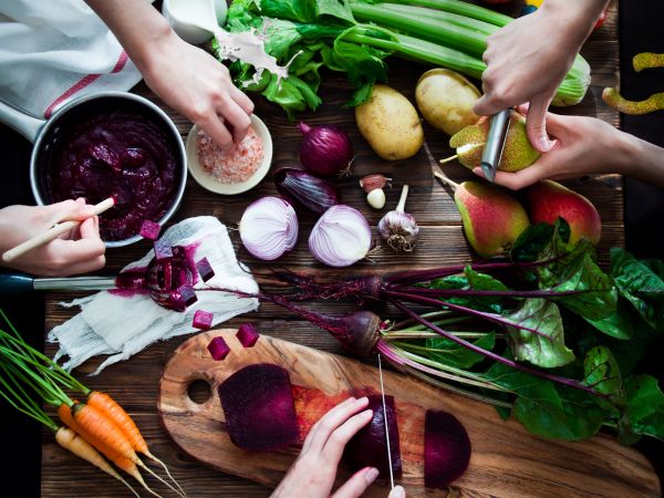 preparing vegetarian meal, chopping beets, peeling pears; potatoes, carrots and celery on a wooden board
