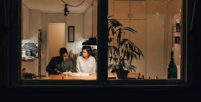 Looking through a dark window frame to a mother and son sat at a table lit with a hanging lamp
