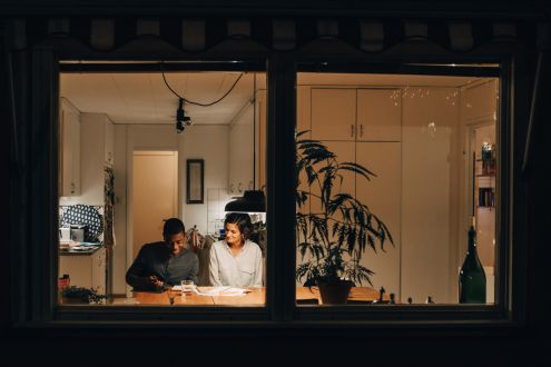 Looking through a dark window frame to a mother and son sat at a table lit with a hanging lamp
