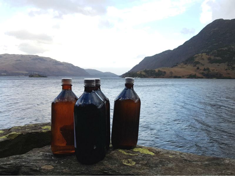 Four full 1-litre bottles placed on a rock next to Ullswater Lake in the Lake District