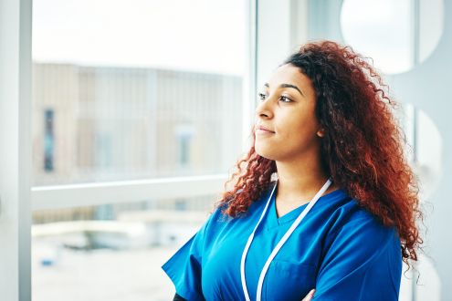 What can I do to stop climate change? A black female nurse looking out a window, deep in thought
