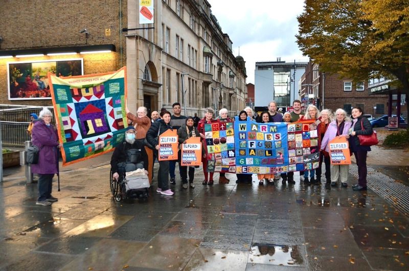 A group of people outside holding up their handmade quilt which reads "warm homes for all" alongside other placards demanding warm homes.
