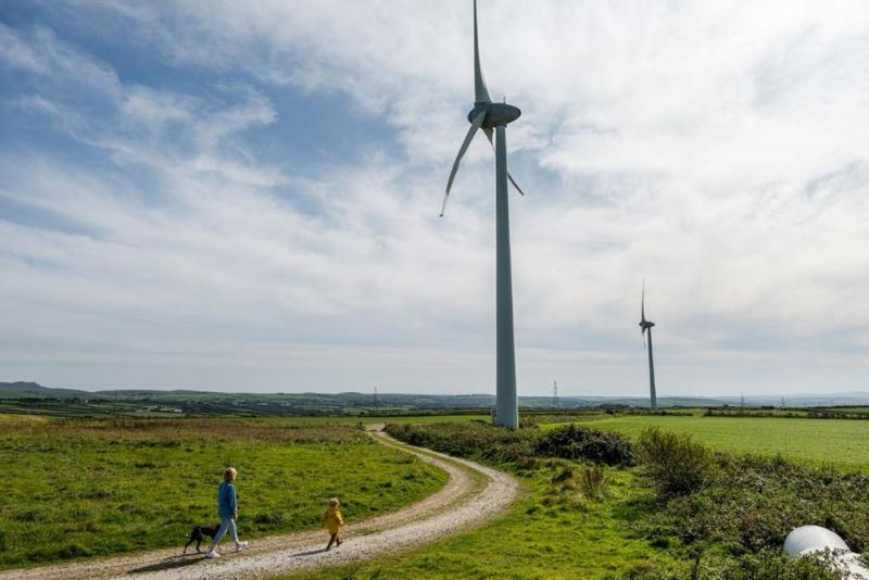 A parent and child walking on a path next to a wind turbine