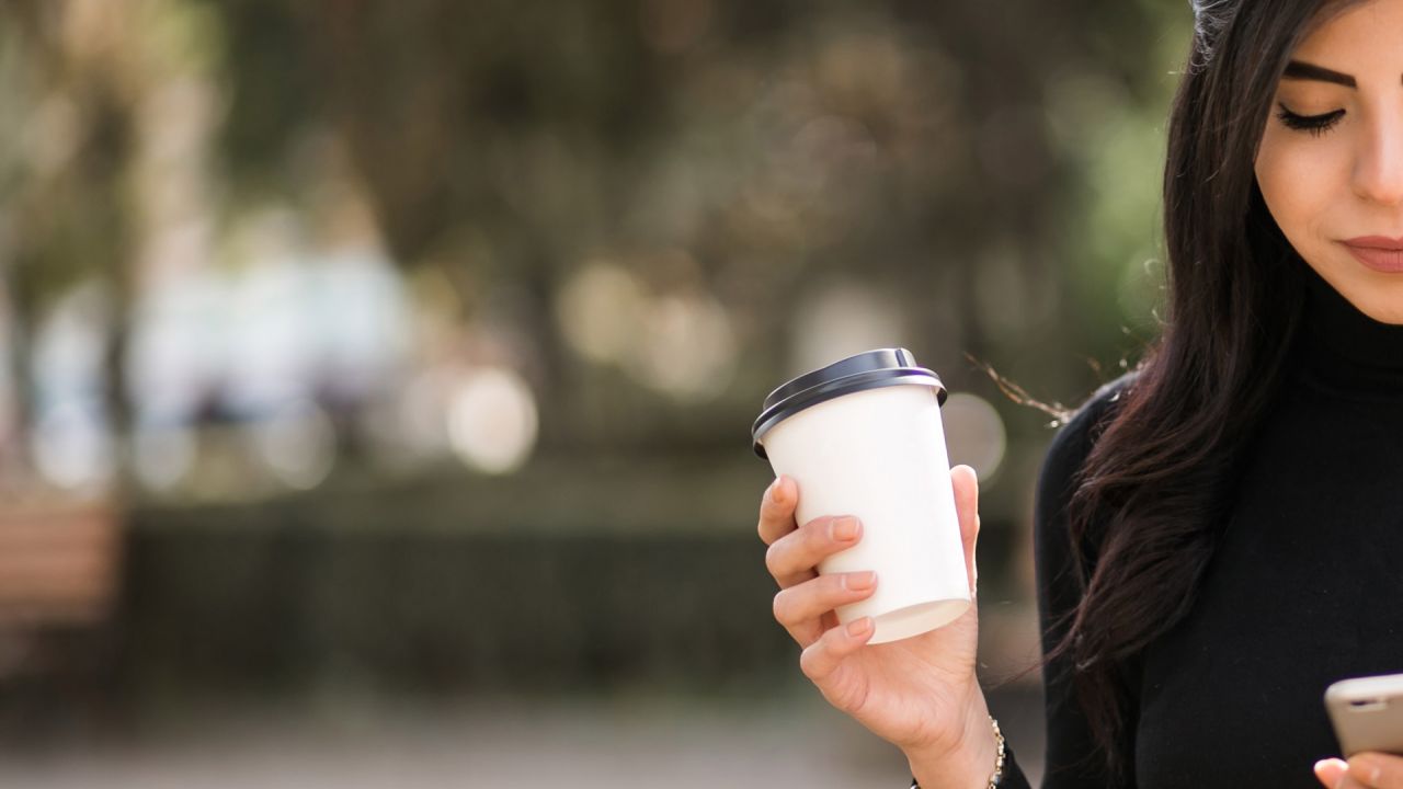Woman holding takeaway cup while looking at phone