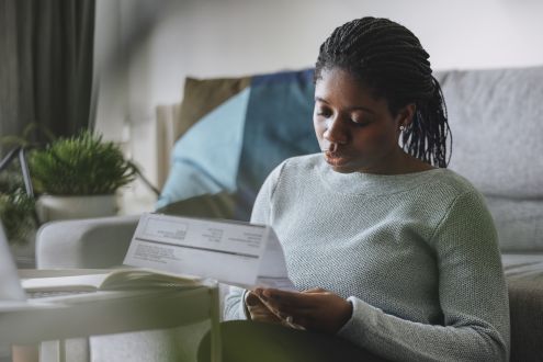 Woman sat by sofa reading paper utility bill